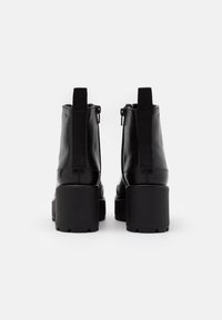 Botas de tobillo de cuero negro con un tacón cuadrado, que cuentan con un cierre de cremallera, paneles laterales elásticos y una textura suave.