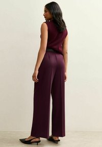 Bordeaux mouwloos topje gecombineerd met brede bordeaux broek en zwarte hakken. Heeft een getailleerde taille met een strakke riemdetail.