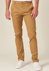 Khaki Chinos aus Baumwollmischung, im Slim Fit, mit flacher Vorderseite und Knopfverschluss. Kombiniert mit weißen Sneakers.