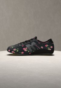 Baskets noires avec motif floral rose, lacets noirs et semelle texturée, présentées sur une surface neutre avec un fond uni.