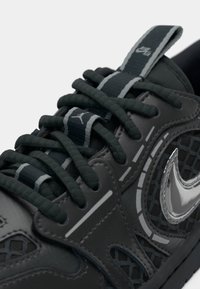 Sive tenisice za sport s teksturiranim sintetičkim materijalom, mrežastim detaljima, debljim vezicama, reflektirajućim Nike logotipom i kontrastnim tamnim elementima.