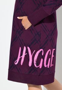 Tunic di cotone viola con motivo a quadri blu; presenta una grafica "HYGGE" rosa, tasca laterale e polsini a coste sull'orlo.