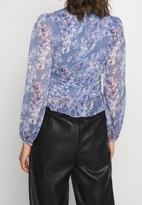 Let, tynd bluse i pastelblå med blomsterprint. Har pufærmer og en flæset kant. Kombineret med sorte læderbukser.