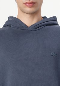 Felpa blu navy con una texture morbida, dotata di una tasca frontale e di un piccolo logo tonale sul petto. Cappuccio regolabile con cordino.