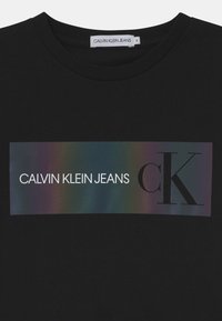 Czarny bawełniany t-shirt z połyskującą prostokątną grafiką z napisem "CALVIN KLEIN JEANS" oraz "ck" w kontrastowych kolorach. Okrągły dekolt.