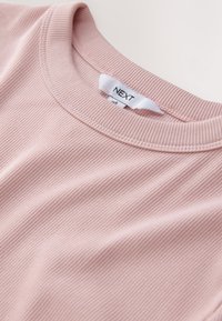 Pink ribbed t-shirt featuring a rounded neckline and visible stitching. Tag shows brand "NEXT" in a small, blue font.