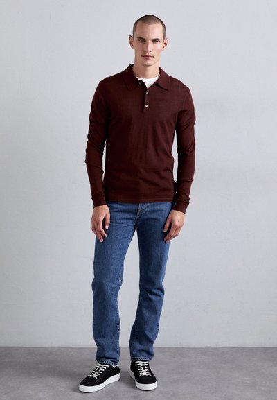 Dunkelbraunes Langarm-Polohemd mit flachem Kragen und drei Knöpfen, kombiniert mit blauen geraden Jeans und schwarzen Sneakers.