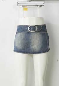 Denim mini krilo z ovalno srebrno zaponko, izbledelo modre barve in zaobljenim robom. Zasnovano z sprednjim žepom in zanko za pas.