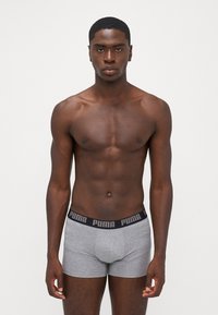 Szürke boxernadrág fekete elastikus derékrésszel, fehér "PUMA" márkázással, sima felülettel és szoros illeszkedéssel. A modell egyenesen áll.