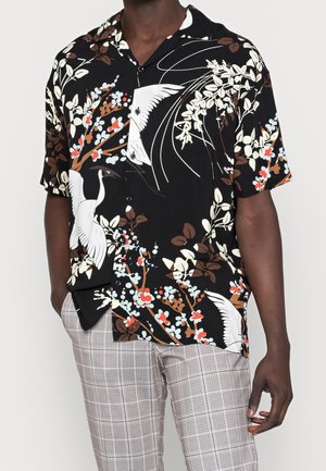 Schwarzes kurzärmeliges Hemd mit Knöpfen, weißen Vögeln und bunten Blumenmustern, getragen zu hellgrauen karierten Hosen.
