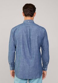 Blauw chambray shirt met lange mouwen, knoopmanchetten, achterste plooi-details en afgeronde zoom. De stoftextuur lijkt lichtgewicht en ademend te zijn.
