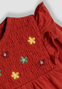 Rotes Baumwollkleid mit gerafftem Oberteil. Mit buntem Blumendruck in Gelb, Grün und Burgunder. Rüschendetail an den Schultern.