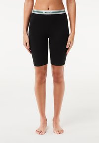 Shorts da bicicletta neri in cotone con una cintura elastica a strisce verde e bianca con il logo "LACOSTE". Texture liscia, design fino al ginocchio.