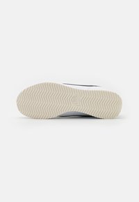 Suola in gomma per sneaker con motivo a spina di pesce; strato esterno bianco lucido; dettagli neri ai lati; logo impressa vicino al tallone.