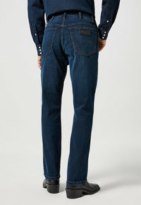 Mörkblå denimjeans med rak skärning, som har två bakfickor och en läderlogotyp. Avslutade med kontrasterande sömmar och en lätt lyster.