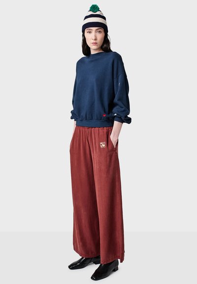 Navyblaues, übergroßes Sweatshirt mit langen Ärmeln, kombiniert mit weit geschnittenen Hosen in Rostfarbe mit einer Tasche. Gestrickte Mütze mit Streifen.