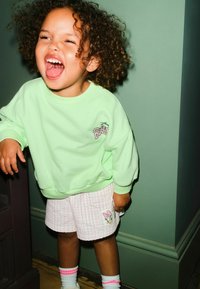 Menta zöld pulóver bordázott mandzsettákkal, fehér kockás rövidnadrággal, melyen hímzett figura látható. Zokni rózsaszín csíkokkal.