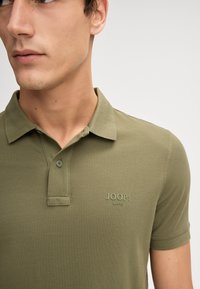 Olijfgroene poloshirt van katoenmix, met een korte kraag, een knoopsluiting met twee knopen en een geborduurd "JOOP! JEANS" logo op de borst.