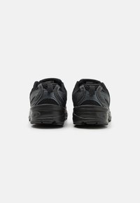 Baskets de sport noires avec des panneaux en maille, des surfaces texturées et une semelle rembourrée. Talon renforcé et détails de marque minimaux à l'arrière.