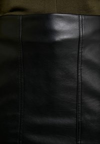 Gonna nera in pelle con una texture liscia, dettagli con cuciture verticali e un design aderente, che trasmette uno stile elegante e contemporaneo.
