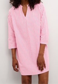 En randig skjortklänning i rosa och vitt med V-hals, 3/4 ärmar och en avslappnad passform; tillverkad av mjukt, andningsbart tyg.