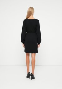 Vestido negro de manga larga con cintura ajustada y corte relajado. Textura suave, con longitud por encima de la rodilla, presenta un escote redondo y puños elásticos.