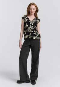 Zwart bloemen top met korte ruches mouwen, voorzien van crèmekleurige en groene bladerenpatronen. Gepaard met losse zwarte jeans en chunky zwarte schoenen.