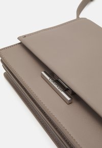 Szürke szintetikus bőr keresztbody táska textúrált felülettel, ezüst kiegészítéssel ellátott Calvin Klein logóval és fedélzáróval.