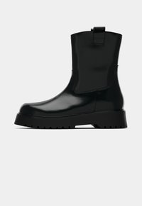 Schwarze Knöchelstiefel mit glänzender Oberfläche, elastischen Seitenpaneelen und einem Zuglasche. Ausgestattet mit einer dicken, strukturierten Sohle für besseren Halt.