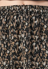 Et svart skjørt med et mønster design som har beige og lysebrune flekker. Det har en elastisk midje og et lett stoff.