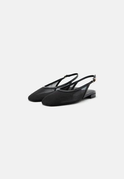 Ballerines slingback noires à bouts pointus, avec fines brides et petites boucles dorées sur les talons, posées sur un fond clair uni.