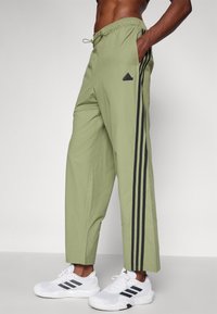 Světle zelené sportovní kalhoty s elastickým pasem, s černými bočními pruhy a vyšitým logem, doplněné o bílé tenisky.