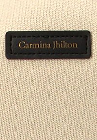 Etiqueta negra con texto dorado "Carmina Jhilon" sobre un fondo de tela beige, mostrando un material texturado y forma rectangular.