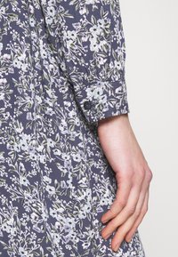 Blusa a fantasia floreale in blu navy, realizzata in morbido cotone. Delicate fiori azzurri e verdi con dettagli ai polsini abbottonati.