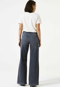 Wijduitlopende denim jeans in een donkere kleur met een hoge taille, voorzien van twee achterzakken en een nette zoom. Gecombineerd met een lichtgekleurde t-shirt.