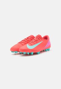 Des crampons de football roses vifs avec une surface texturée, des accents turquoise et une marque exagérée sur le côté. Six crampons pour l'adhérence.