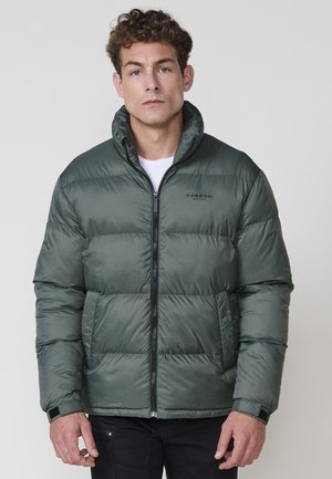 Chaqueta acolchada de color verde oscuro con un alto cuello, cierre frontal con cremallera y diseño de costuras horizontales. Presenta un logo en el pecho y puños elásticos.
