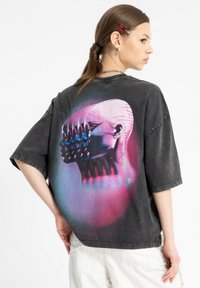 Czarna, oversize koszulka z grafiką przedstawiającą stylizowaną głowę z wieloma twarzami w żywych kolorach na plecach.