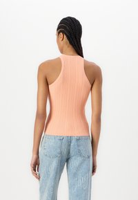 Top a canotta a coste color pesco con un design aderente, caratterizzata da spalline larghe e una schiena dritta. Abbinata a jeans in denim azzurro chiaro.