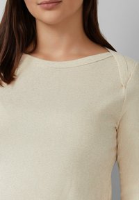 Beige geribde lange mouw top met een open halslijn; heeft een licht asymmetrisch schouderontwerp en een zachte, gestructureerde stof.