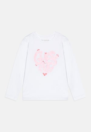 T-shirt bianco a maniche lunghe con un design di cuore rosa scintillante, testo "GUESS" e "1981", scollatura rotonda, texture di tessuto morbido.