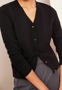 Cardigan negru, fabricat dintr-un material moale, cu decolteu în V, mâneci lungi și închidere cu butoane de culoare aurie. Design ajustat, cu manșete canalate.