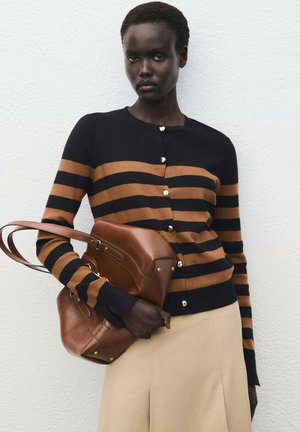 Marinblauer und braun gestreifter Cardigan mit goldenen Knöpfen und langen Ärmeln. Das Model hält eine braune Ledertasche. Ein schlichter beiger Rock rundet den Look ab.