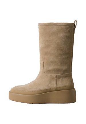 Bota beige de ante hasta media pantorrilla con suela gruesa de plataforma de goma y lengüeta trasera, con el sutil logo "ck" cerca del borde superior.