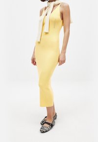 Robe en tricot côtelé jaune au design ajusté, longueur mi-mollet, avec un décolleté arrondi. Associée à des ballerines à rayures noires et blanches.