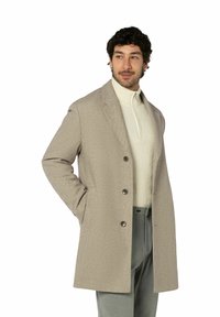 Hellbeiger Wollmantel mit aufgeschlagenem Kragen, einreihigem Design und drei Knöpfen. Trägt man über einem cremefarbenen Rollkragenpullover.