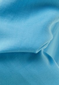Světle modrá tkanina s viditelnou texturou vazby, jemně složená a pomačkaná, ukazuje hladký, ale mírně nerovný povrch.