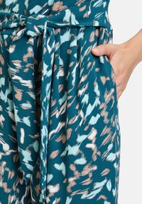 Teal színű overall világoskék és barack színű absztrakt mintákkal. Derékban megkötős, oldalzsebes, sima anyagú.