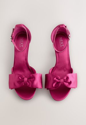 Roosad satiinsed kontsakingad, mille eesosas on lai lipsu detail ja pahkluu rihm. Sile tekstuur ja avatud varvastega disain. Nähtav minimalistlik bränding.