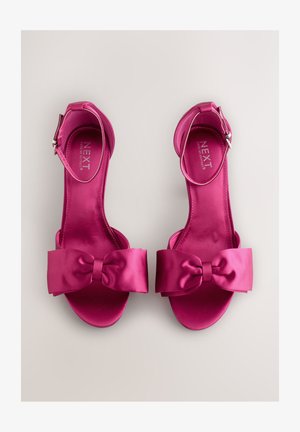 Rosa satinsandaletter med klack, bred rosettdetalj framtill och ankelrem. Slät textur och öppen tå-design. Minimalistisk märkning synlig.